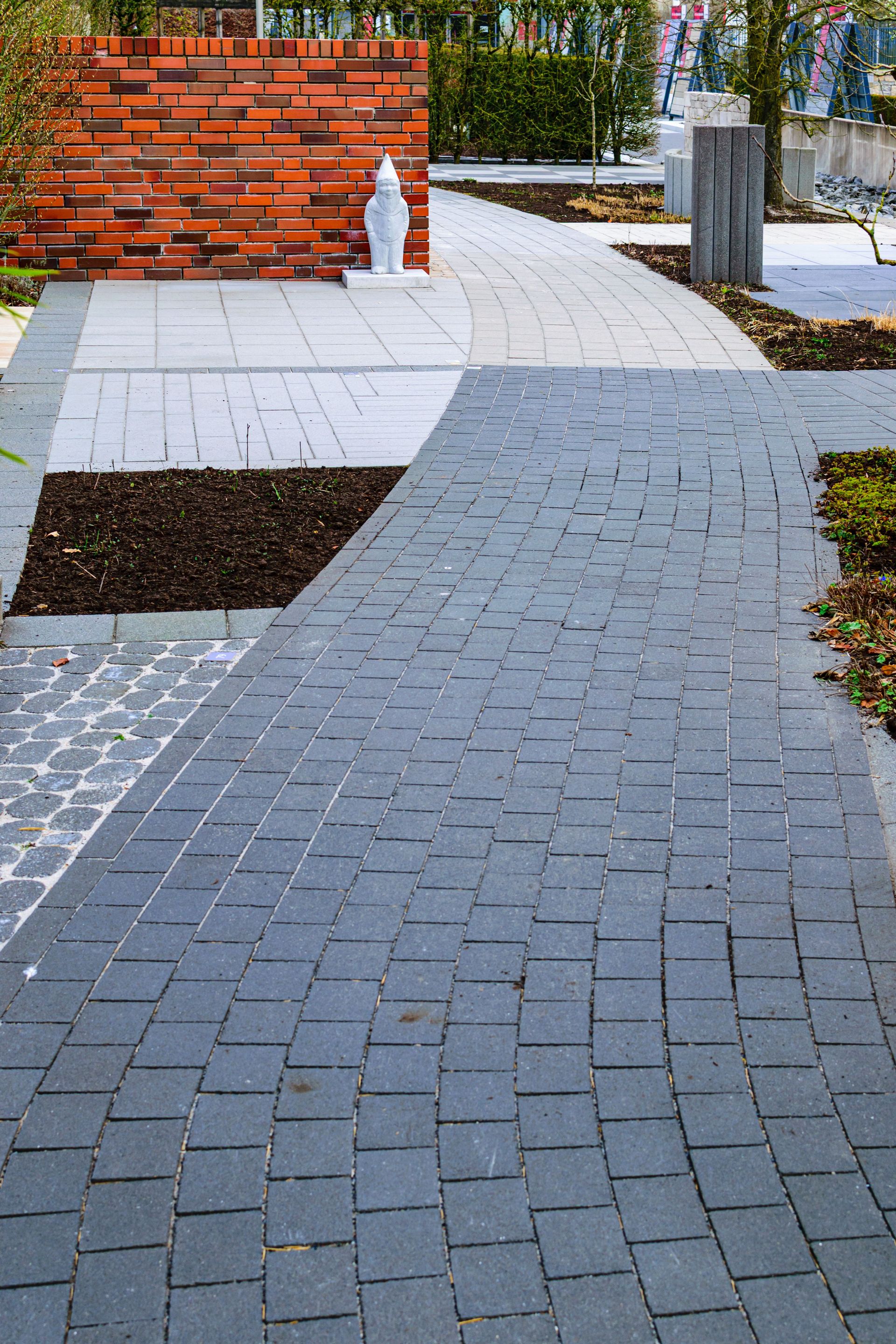 A curved brick pathway in a modern urban garden with red bricks and greenery.