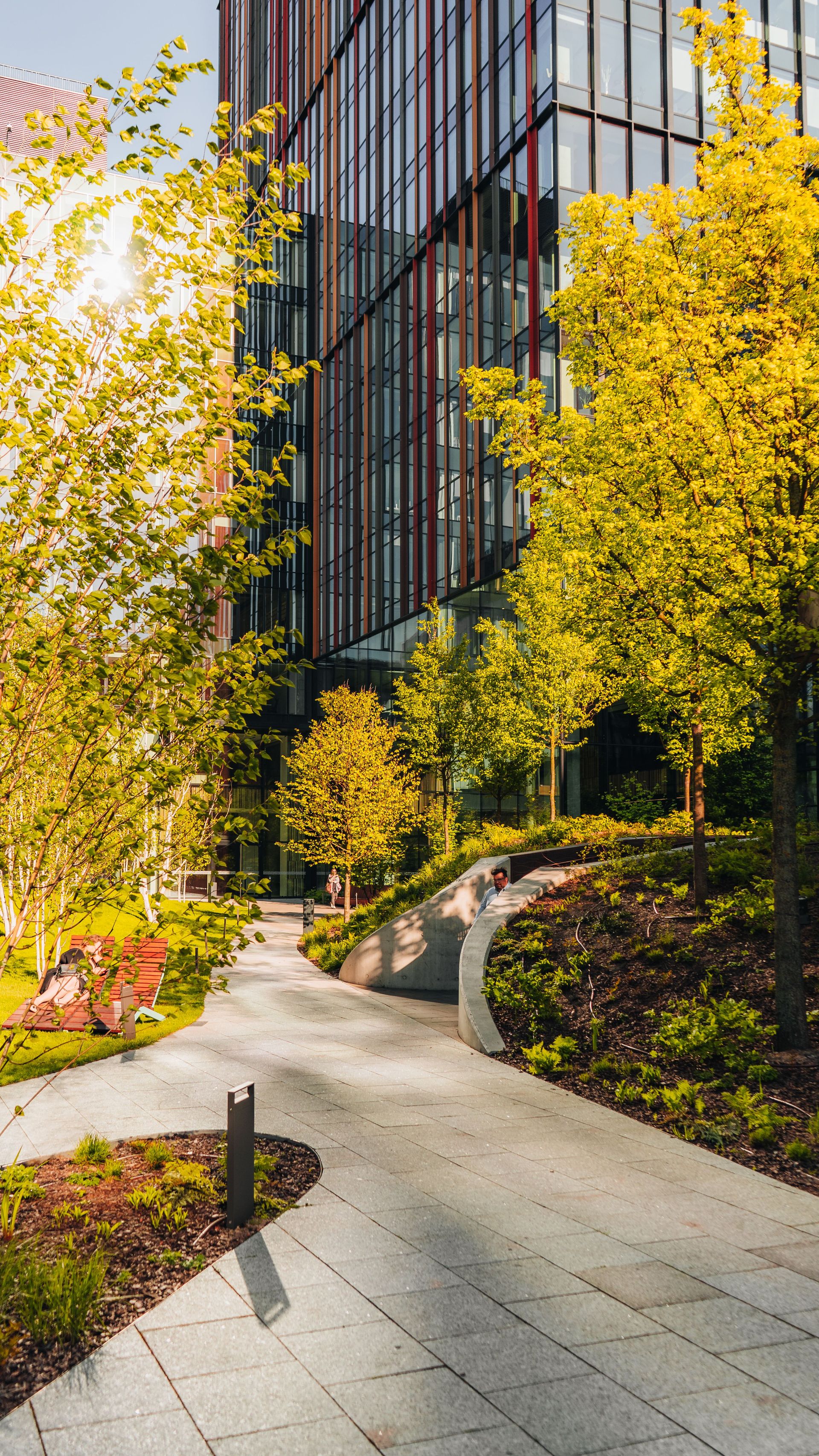 A modern office building surrounded by vibrant autumn foliage and a paved pathway in an urban setting.