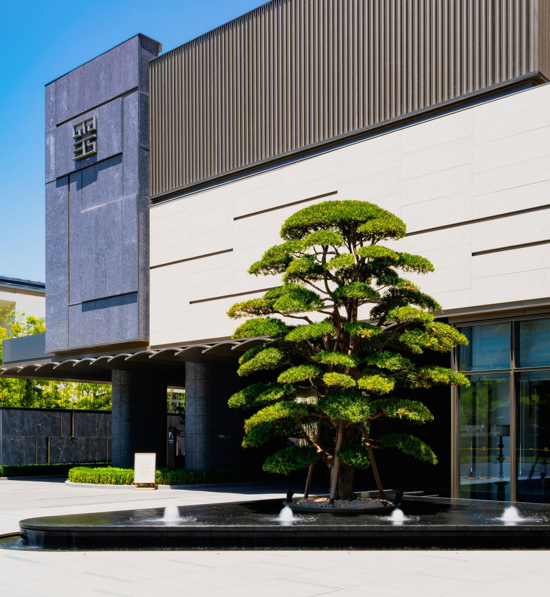 Modern building entrance with a sculpted tree and fountain.